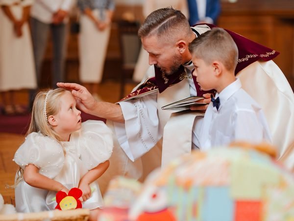 Kunigas bažnyčioje laimina mergaitę ir berniuką baltais drabužiais – krikštynų fotosesija Šiauliuose