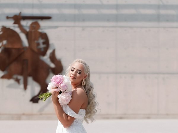 Nuotaka su rausvų pijonų puokšte pozuoja prie paminklo – vestuvių fotosesija Šiauliuose