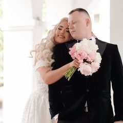 Jaunieji apsikabinę stovi arkadoje, nuotaka laiko rausvų gėlių puokštę – Donatos Jankauskės fotografija, Šiauliai
