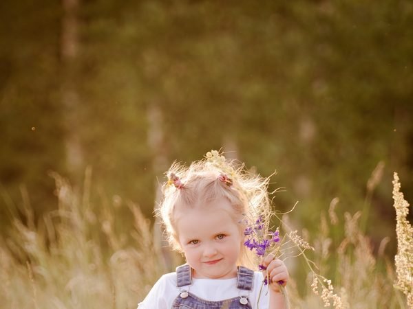 Mergaitė aukštoje žolėje laiko violetinių lauko gėlių puokštelę – vaikų fotosesija Šiauliuose