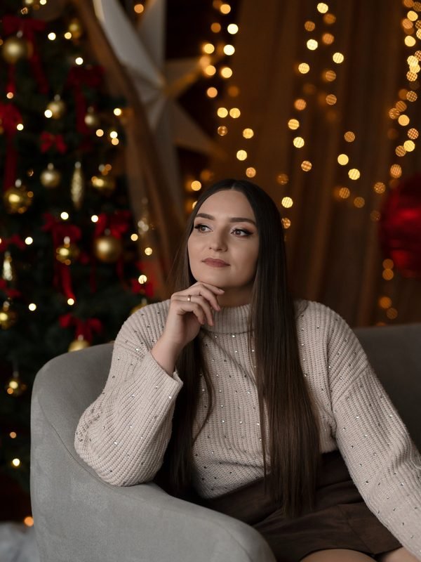 Moteris sėdi fotelyje kalėdinių žibučių ir eglutės fone – kalėdinė fotosesija Šiauliuose