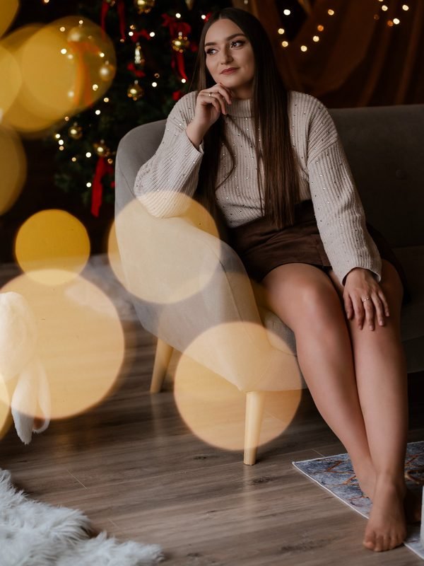 Moteris sėdi fotelyje prie kalėdinės eglutės ir žibančių lempučių – kalėdinė fotosesija Šiauliuose