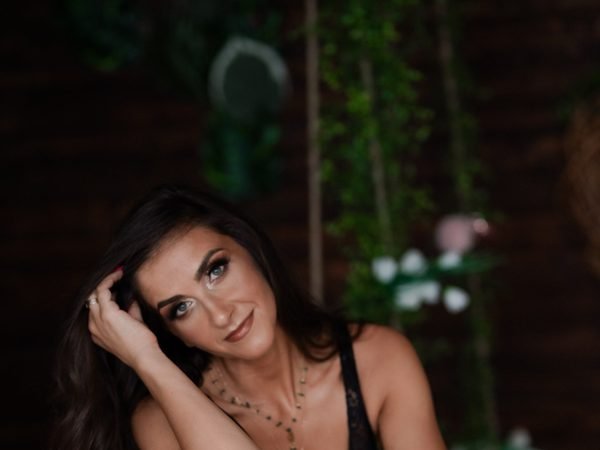 Moters portretas tamsiame fone su žalumynais, ranka prie plaukų – asmeninė fotosesija Šiauliuose