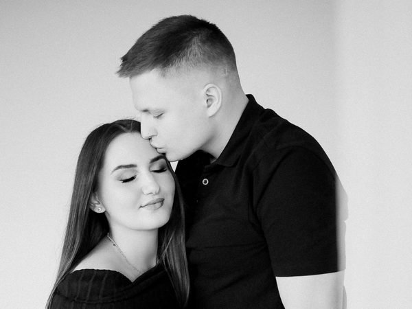 Vyras švelniai bučiuoja moterį į kaktą studijoje – laukimo fotosesija Šiauliuose