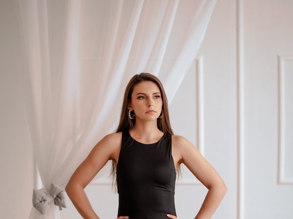 Moteris stovi studijoje juoda suknele, rankos ant klubų – asmeninė fotosesija Šiauliuose