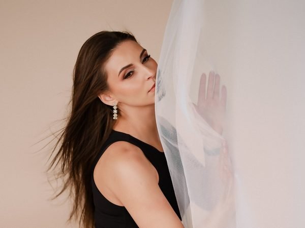 Moteris juoda liemenėle žvelgia pro skaidrų audinį studijoje – asmeninė fotosesija Šiauliuose