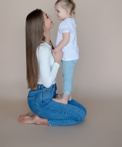 Mama klūpo priešais stovinčią mažametę dukrą studijoje – šeimos fotosesija Šiauliuose