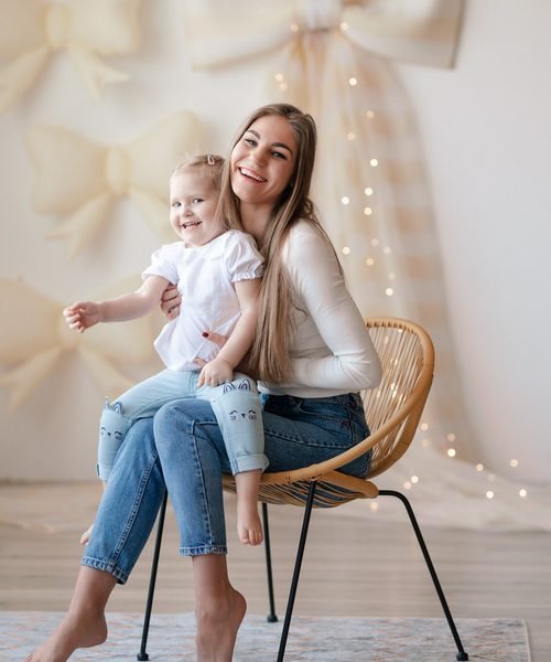 Mama su mažąja dukra sėdi ant pintinio krėslo, aplinkui puošybos kaspinai – šeimos fotosesija Šiauliuose