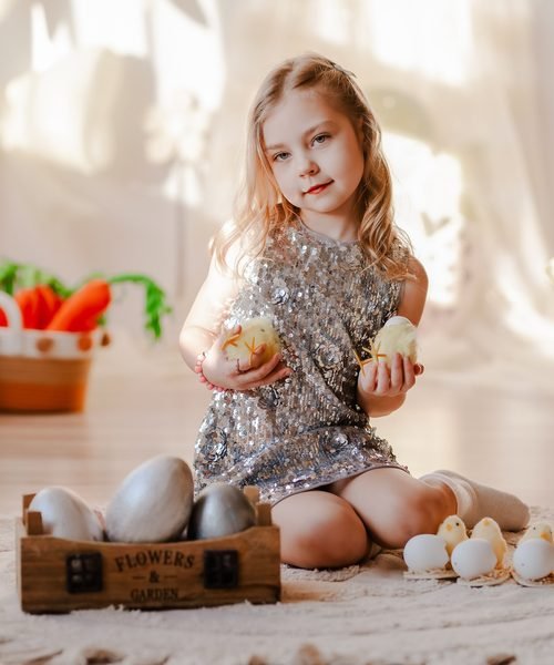 Mergaitė sidabrine suknele laiko mažus viščiukus prie dekoruotų kiaušinių – vaikų fotosesija Šiauliuose