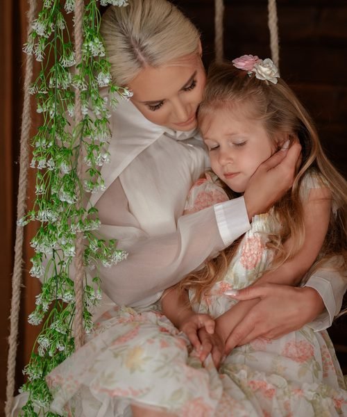 Mama apkabinusi dukrą sūpynėse, papuoštose žalumynais ir gėlytėmis – šeimos fotosesija Šiauliuose