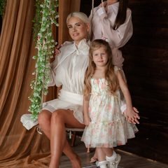 Moterys su mergaite pozuoja prie sūpynių, aplinkui kabo gėlių girlianda – Donatos Jankauskės fotografija, Šiauliai
