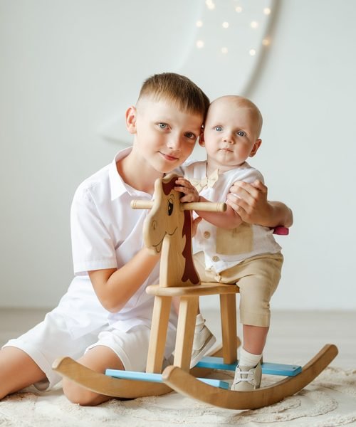 Berniukas laiko kūdikį ant medinio žirgelio žaislo – krikštynų fotosesija Šiauliuose