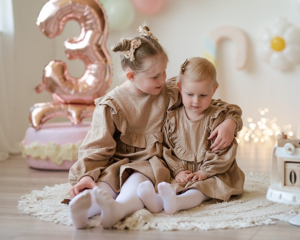 Dvi mažametės apsikabinusios sėdi šalia gimtadienio balionų – cake smash fotosesija Šiauliuose