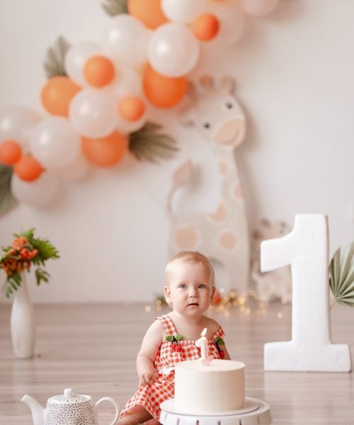 Kūdikė sėdi šalia gimtadienio torto, fone skaičius vienas ir balionai – cake smash fotosesija Šiauliuose