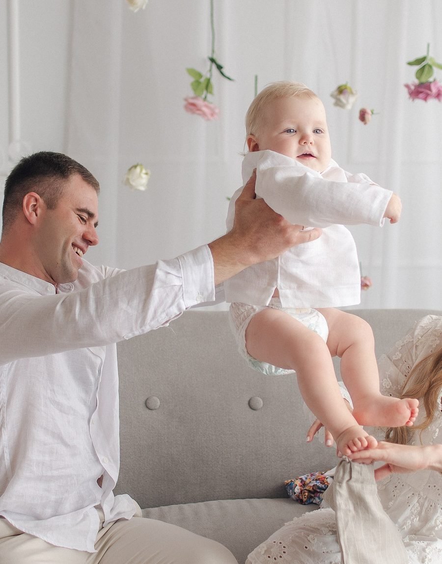 Tėtis linksmai kelia kūdikį į orą tarp kabančių gėlių – Donatos Jankauskės fotografija, Šiauliai