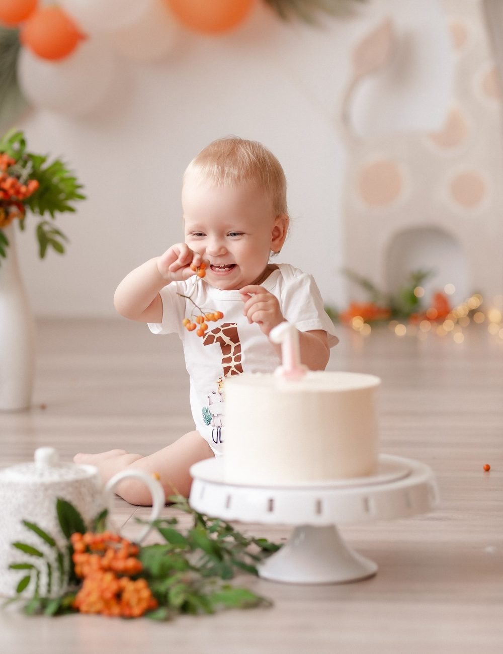 Kūdikis besijuokdamas valgo uogas šalia gimtadienio torto, fone balionai – cake smash fotosesija Šiauliuose