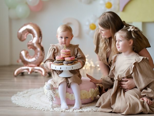 Mergaitė laiko spurgų tortą, šalia mama ir sesuo stebi – šeimos fotosesija Šiauliuose