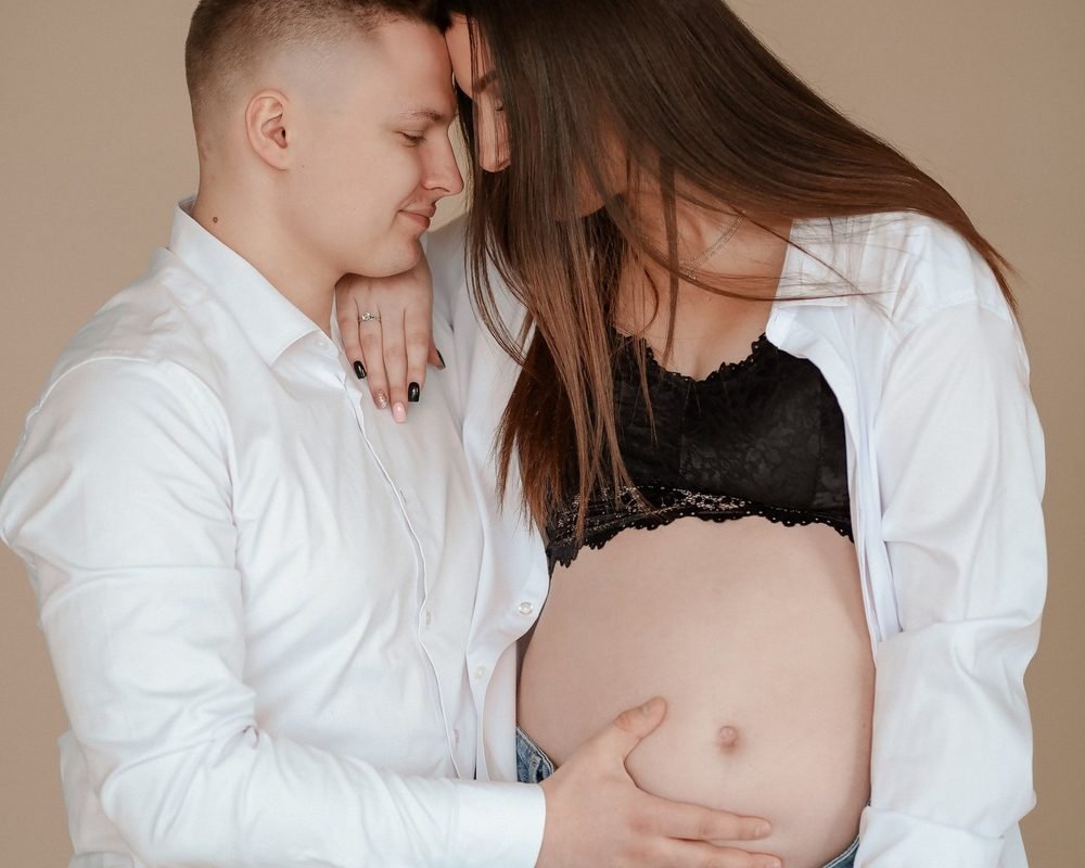 Vyras meiliai apkabina nėščią moterį, bučiuoja jos galvą – laukimo fotosesija Šiauliuose