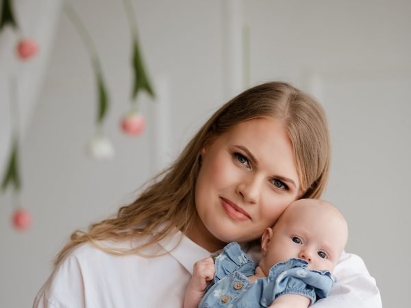 Moteris laiko ant rankų kūdikį džinsiniu kostiumėliu – šeimos fotosesija Šiauliuose