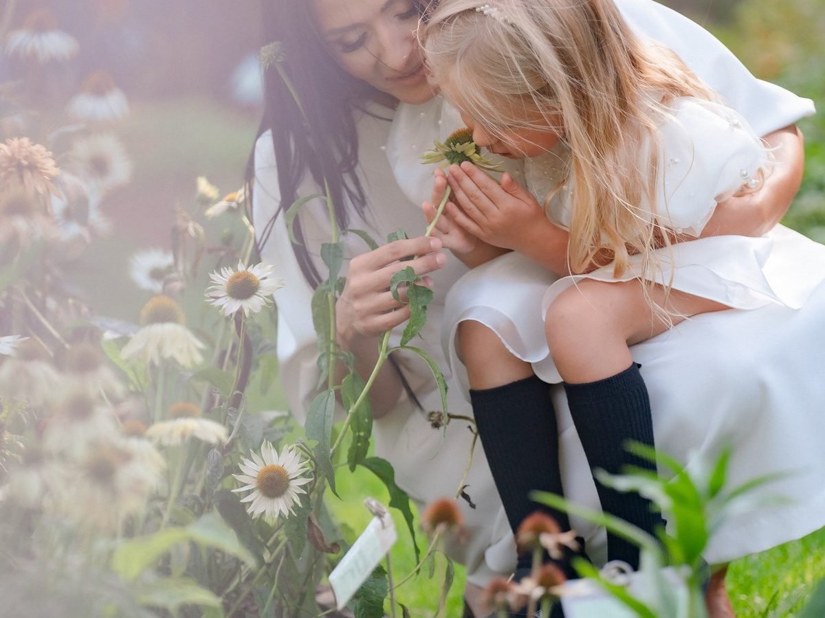 Mama su dukra sode kartu uosto baltą gėlę, abi dėvi baltus drabužius – krikštynų fotosesija Šiauliuose